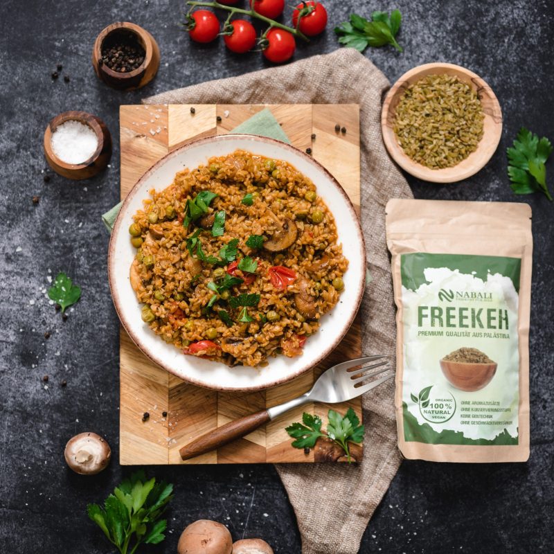 Freekeh Gericht mit Gemüse und Kräutern Ein Teller Freekeh mit Gemüse und Kräutern, umgeben von frischen Zutaten und einer Packung Freekeh.